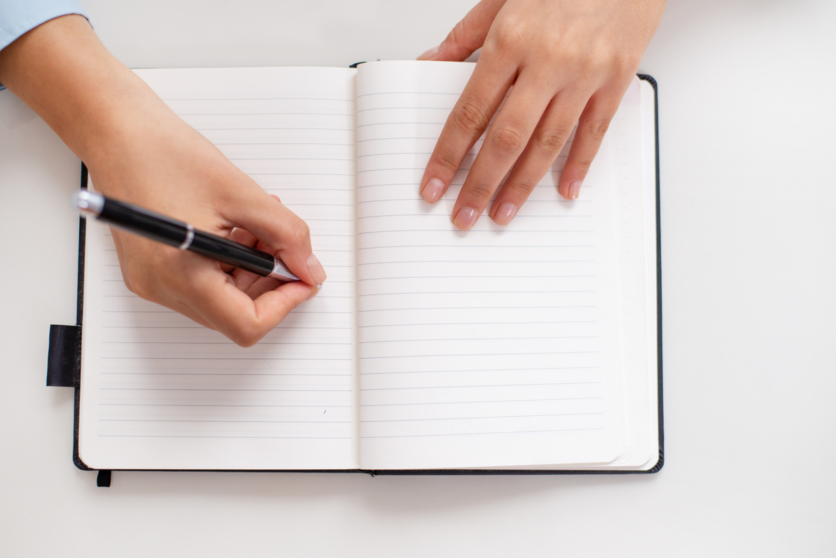 Top view of female hands writing in notebook on desk